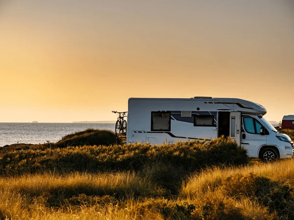 Motorhome parked by the sea at sunset, with bicycles attached, surrounded by windswept grass. RV Lifestyle Experts