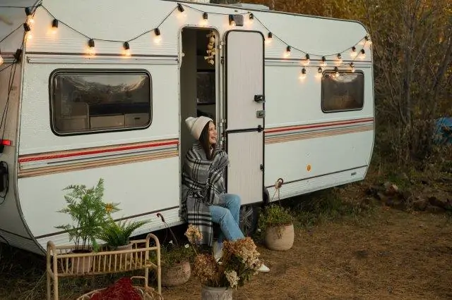 A woman is sitting in front of a camper trailer. Solar Power Heater for RV. RV Lifestyle Experts
