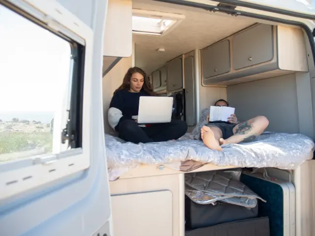 A woman and a man sitting on a bed with a laptop and a book, browsing RV Shows in California. RV Lifestyle Experts
