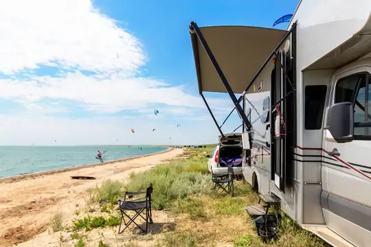 Recreational vehicle parked by the seaside with kitesurfers in the distance. RV Lifestyle Experts