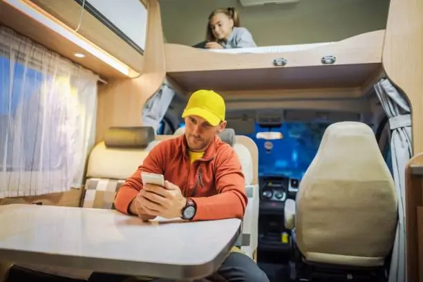 Man using smartphone in a camper van with a child in the overhead bunk. RV Lifestyle Experts